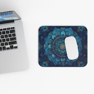 May include: A rectangular mousepad with a detailed blue and gold mandala design. A white computer mouse rests on the pad, next to a laptop keyboard. The mandala features intricate floral patterns and a circular center.