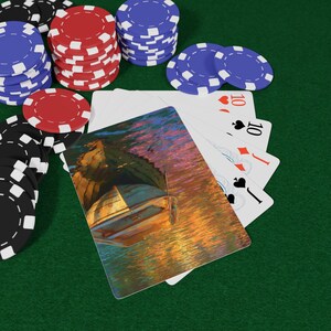 May include: A selection of poker chips in red, black, and blue, alongside playing cards. The cards feature a boat on water. The cards display the number 10 and the suits of hearts, diamonds, and spades. The background is green.