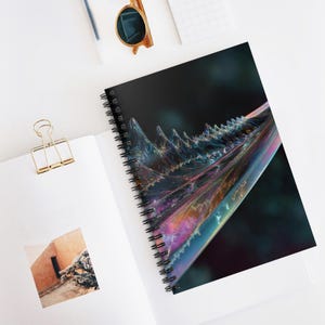 Può includere: Quaderno a spirale con un design astratto e iridescente. La copertina presenta un motivo colorato con forme cristalline su uno sfondo scuro. Il quaderno è aperto, rivelando pagine bianche e una piccola foto.