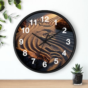 May include: A round wall clock with a black frame and a face featuring a photograph of raked sand in a zen garden with large rocks. The clock has white numbers from 1 to 12 and thin black hour, minute, and second hands centered on the dial.
