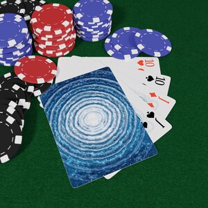 May include: Poker chips in black, red, and blue are stacked on a green surface, alongside playing cards. One card features a blue and white spiral design. The cards show the number 10 and the suits of hearts, diamonds, and spades.