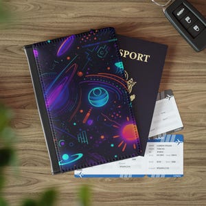 Può includere: Un porta passaporto nero con un vivace design a tema spaziale con pianeti, stelle e forme geometriche in colori neon. Un passaporto nero e due carte d'imbarco sono accanto al porta passaporto. È visibile anche una chiave dell'auto.