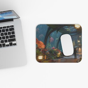May include: A rectangular mousepad featuring a fantasy landscape with orange, pink, and green flora. A white computer mouse sits on the pad, next to a laptop. The scene includes a person standing in a pathway with arched structures and hanging lights.