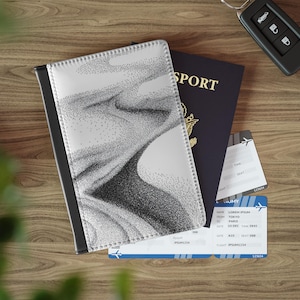 May include: A passport cover with a black and white abstract design, a dark blue passport, and two airline tickets are arranged on a wooden surface. A car key is also present. The passport cover has a black border and a dotted pattern.