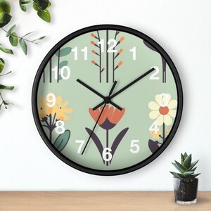 May include: A round wall clock with a black frame and a light green face. The clock face features floral illustrations in yellow, orange, and white, with black clock hands and white numerals. The clock is on a wooden surface.
