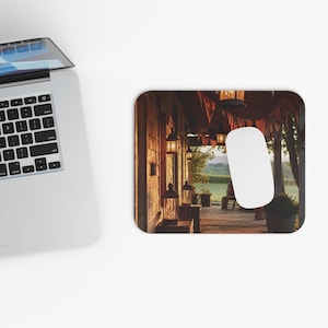 Peut inclure: Un tapis de souris rectangulaire représentant une scène de porche rustique avec des lanternes suspendues et une souris d'ordinateur blanche. Le porche en bois dégage une lueur chaleureuse, avec un champ visible en arrière-plan. Le tapis de souris est à côté d'un ordinateur portable.