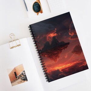 May include: A spiral-bound notebook featuring a dramatic landscape of floating islands and a fiery sunset. The cover art showcases a vibrant scene with dark clouds and a bright orange sky. The notebook is open, revealing blank pages.