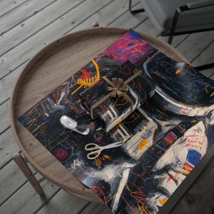 May include: A wrapped present with a brown ribbon sits on abstract patterned wrapping paper. The paper and gift box have a dark background with colourful brushstrokes. Scissors and tape are also on the table, which is made of wood.