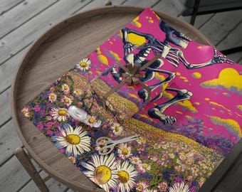May include: A gift wrapped in pink paper featuring a running skeleton illustration with yellow and blue accents. The gift is tied with a brown ribbon and sits atop a floral patterned wrapping paper with daisies. Scissors and tape are also visible.