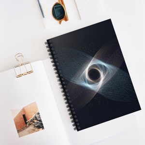 May include: Spiral-bound notebook with a black cover featuring a geometric design of swirling white and blue lines around a central gold circle. The notebook is open, revealing white pages and a gold paper clip.