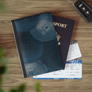 May include: A passport cover with a blue and black spiral design, a dark blue passport, and two boarding passes are on a wooden surface. A car key fob is in the upper right corner. The passport cover is open, revealing the passport.