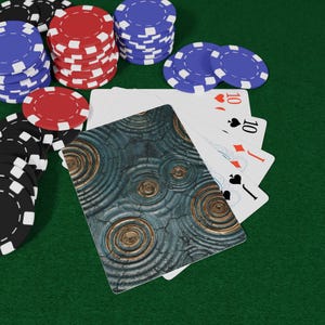 May include: Poker chips in black, red, and blue are stacked on a green felt surface. Playing cards with the number 10 are fanned out, with a card featuring a textured, circular design. The scene suggests a game of poker.