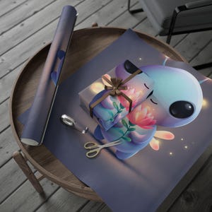 May include: A rectangular gift box wrapped in paper featuring a cartoon alien holding a pink lotus flower, tied with a brown ribbon. Beside the box lies a roll of matching wrapping paper, a small roll of clear tape, and silver metal scissors.