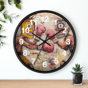 Könnte beinhalten: Schwarz gerahmte Wanduhr mit einem abstrakten Gemälde von zwei Boxern mit rosa Handschuhen. Das Zifferblatt hat weiße Zahlen und schwarze Zeiger. Das Kunstwerk verwendet Gelb-, Rot- und Brauntöne.
