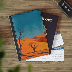 Op de afbeelding: Een paspoorthoes met een woestijnlandschap, een donkerblauwe paspoort en twee instapkaarten liggen op een houten oppervlak. De hoes heeft een blauwe lucht, een oranje woestijn en kale bomen. Een autosleutel is ook aanwezig.