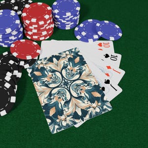Könnte beinhalten: Ein Pokerspiel-Setup mit Spielkarten und Pokerchips. Die Karten haben ein florales Design auf der Rückseite. Stapel von roten, blauen und schwarzen Chips sind sichtbar. Die Karten zeigen die Zehn der Herzen, die Zehn der Diamanten und den Buben der Pik.