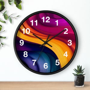May include: Circular wall clock with a black frame. The clock face has a colourful, abstract design with swirling bands of purple, orange, yellow, and blue. White numerals mark the hours. The clock hands are black.