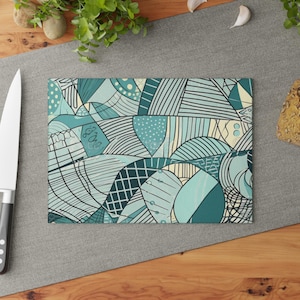 Könnte beinhalten: Ein rechteckiges Glasschneidebrett mit einem komplexen abstrakten Muster aus türkisfarbenen, hellblauen und cremefarbenen Linien, Gittern und Punkten. Das Design besteht aus verschiedenen geometrischen Formen und geschwungenen Segmenten.