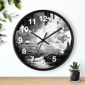 May include: A round wall clock with a black frame and a black and white abstract digital glitch art face. The clock features white sans-serif numerals from 1 to 12 and black hour, minute, and second hands centered on the dial.