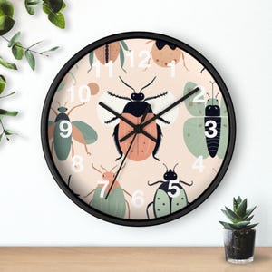 May include: Round wall clock with a black frame and a light peach background. The clock face features various cartoon insects in shades of green, orange, and brown. White numbers mark the hours. The clock hands are black.
