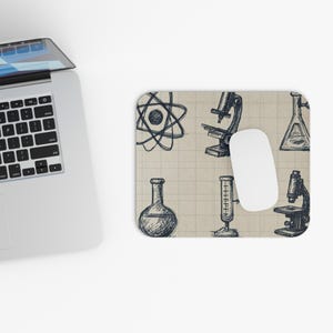 Pode incluir: Um mousepad retangular com fundo bege e tema científico. O design apresenta ilustrações desenhadas à mão de equipamentos de laboratório, incluindo um microscópio, frascos e um símbolo de átomo. Um mouse branco está no mousepad.