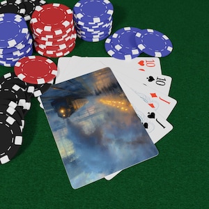 Puede incluir: Juego de póquer sobre una superficie de fieltro verde. Montones de fichas de póquer rojas, azules y negras rodean una mano de cartas. Las cartas muestran una ilustración de un tren y el número 10.