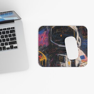 Op de afbeelding: Rechthoekige muismat met een kleurrijk, abstract schilderij van een astronaut. Het kunstwerk bevat een helm met gekrabbelde tekst en een Amerikaanse vlagpatch. Een witte computermuis ligt op de mat.