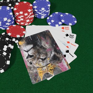 Puede incluir: Una escena de juego de póquer con cartas y fichas de póquer. Las cartas muestran la cara de un león con una corona dorada. Pilas de fichas rojas, azules y negras están dispuestas sobre una superficie de fieltro verde. Las cartas muestran el número 10 y una jota.