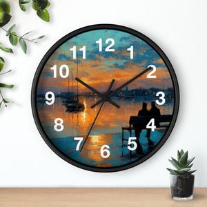 Può includere: Un orologio da parete rotondo con cornice nera e numeri bianchi. Il quadrante presenta un dipinto impressionista di un tramonto su un porto con barche e due figure sedute su una panchina, in vivaci tonalità di arancione, blu e verde acqua.