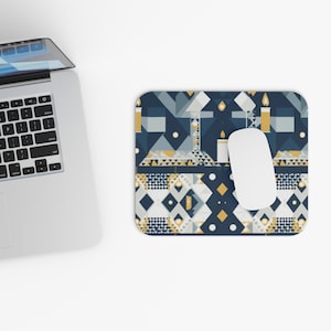 Könnte beinhalten: Rechteckiges Mauspad mit einem geometrischen Muster in Marineblau, Gold und Weiß. Das Design umfasst Formen, die Kerzen und abstrakten Formen ähneln. Eine weiße Computermaus liegt auf dem Pad, neben einem Laptop.