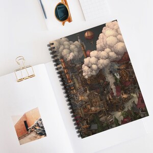 May include: Spiral-bound notebook with a steampunk city illustration, featuring airships, factories, and clouds. The cover art depicts a detailed, colourful cityscape with a fantasy theme. The notebook is open on a white surface.