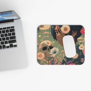 May include: A rectangular mouse mat with a floral and skull design and an anime-style character. The mouse mat has a green background with a skull and flowers. A white computer mouse is on the right side of the mouse mat.