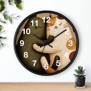 May include: A round wall clock with a black frame. The clock face features two hugging cartoon cats, one green and one white with brown spots. The clock hands are black, and the numbers are white.