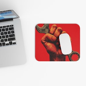 Könnte beinhalten: Rotes Mauspad mit einer detaillierten Illustration einer Hand, die einen Schraubenschlüssel greift. Eine weiße Computermaus befindet sich auf der rechten Seite. Das Bild hat eine Vintage- und Industrieästhetik mit Fokus auf Mechanik und Werkzeuge.