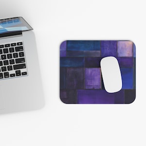 Könnte beinhalten: Ein rechteckiges Mauspad mit einem geometrischen Design in Blau- und Lilatönen. Eine weiße Computermaus liegt auf dem Mauspad, neben einem Laptop.