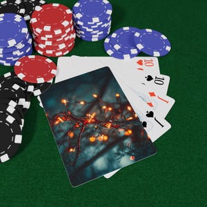 Puede incluir: Fichas de póquer negras, rojas y azules apiladas sobre una superficie verde, junto a naipes. Las cartas muestran el número 10 y una jota, con palos de corazones, diamantes y picas. Una carta presenta una foto de luces de hadas.