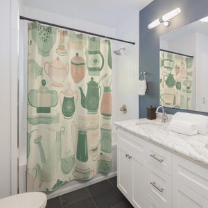Pode incluir: Uma cortina de duche com um padrão repetitivo de vários utensílios de cozinha, incluindo bules, açucareiros e jarros em tons de verde salva, rosa suave e creme. O design está impresso num tecido de fundo de cor creme claro.