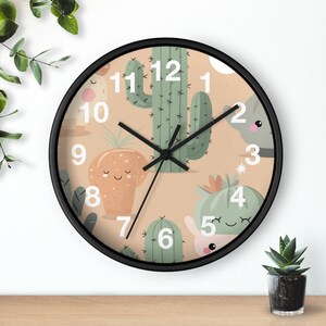 May include: A round wall clock with a black frame featuring a beige background with cartoon cacti and succulents. The clock hands are black, and the numbers are white. The clock is a decorative item.