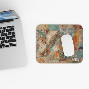 May include: A rectangular mousepad with a patchwork design in shades of beige, brown, teal, and orange. A white computer mouse rests on the pad. A laptop is partially visible in the upper left corner.