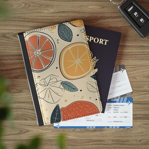 May include: A passport cover with a citrus fruit design, a dark blue passport, and two boarding passes are on a wooden surface. The passport cover features orange slices and green leaves. A car key is also visible.