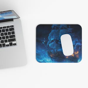 May include: A rectangular mousepad featuring a dramatic illustration of a tall ship sailing through a stormy sea. The artwork is predominantly blue and dark, with a white mouse positioned on the right side. The design evokes a sense of adventure and nautical themes.