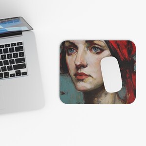 May include: A rectangular mousepad featuring a portrait of a woman with red hair and blue eyes. The artwork has a painterly style with a teal background. A white computer mouse is positioned on the right side of the mousepad.