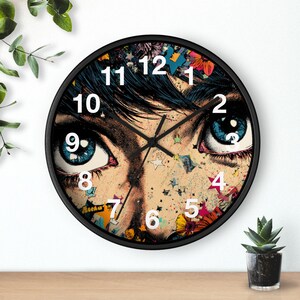 May include: Black round wall clock featuring a pop art style image of a person's eyes with blue irises. The clock face has white numerals and hands. Colorful stars and floral accents decorate the face.