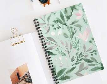May include: A spiral-bound notebook with a floral design. The cover features a light green background with a pattern of green, gray, and pink leaves and flowers. The notebook is open, revealing blank white pages.
