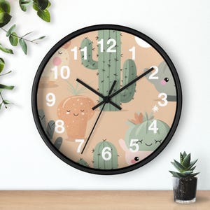 May include: A round wall clock with a black frame and a beige face featuring a pattern of green and orange cartoon cacti with smiling faces. The clock has white numbers from 1 to 12 and three black hands indicating the time against the illustration.