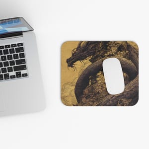May include: A rectangular mousepad featuring a detailed illustration of a dragon coiled around a stone structure. The dragon is dark, with intricate scales and a menacing expression. A white computer mouse rests on the pad.