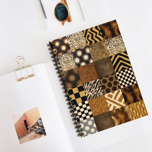 Op de afbeelding: Spiraalgebonden notitieboek met een patchwork ontwerp met verschillende dierenprint patronen in bruin, zwart en tan tinten. Het notitieboek ligt open op een wit oppervlak, met een gouden paperclip en zonnebril in de buurt.