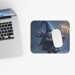 May include: A rectangular mouse mat with a fantasy illustration of a gnome in a blue wizard hat, holding a menorah. The design is set against a dark blue, snowy background. A white computer mouse is on the mouse mat.