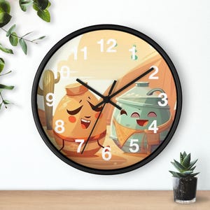 Könnte beinhalten: Eine runde Wanduhr mit schwarzem Rahmen. Das Zifferblatt zeigt eine Cartoon-Illustration von zwei lächelnden Figuren in einer Wüstenlandschaft. Die Zeiger sind schwarz und die Zahlen weiß.