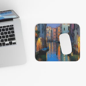 Peut inclure: Tapis de souris rectangulaire avec une peinture d'une scène de canal. L'œuvre d'art représente des bâtiments et des bateaux, avec une palette de couleurs chaudes de bleus, de jaunes et d'oranges. Une souris d'ordinateur blanche est sur le côté droit.